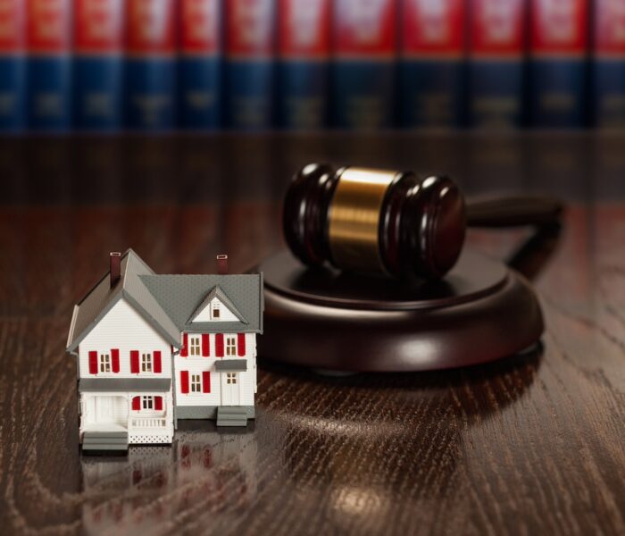 Gavel and Small Model House on Wooden Table With Law Books In Background. 